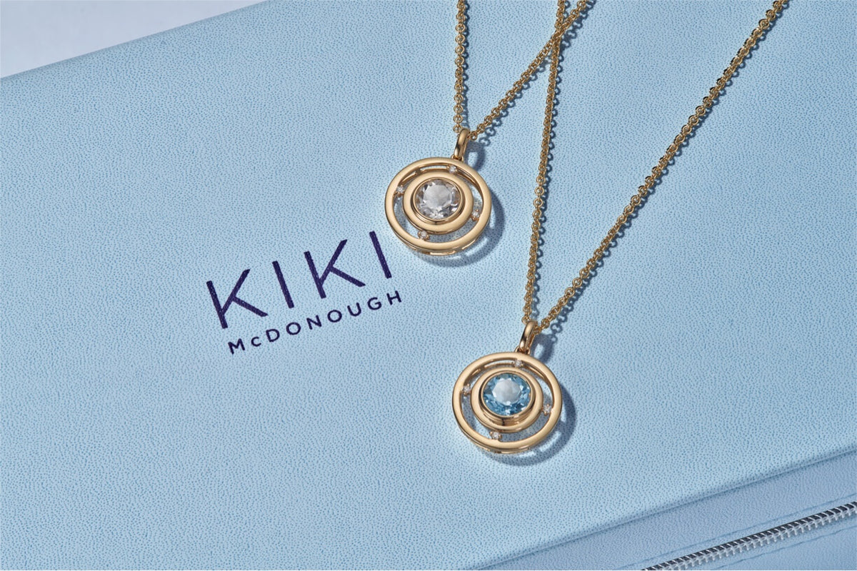 Two gold necklaces with pendants on a light blue surface with 'KIKI McDonough' branding.